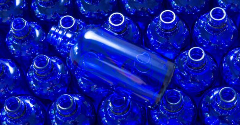 A large quantity of cobalt blue glass bottles stacked next to each other with one blue glass bottle sitting on top of them.