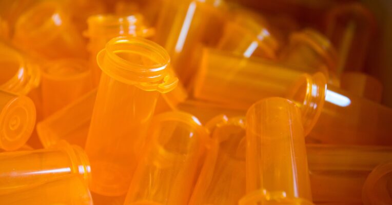 A bulk selection of blank orange prescription pill bottles lay piled on top of each other. They don't have labels or caps.