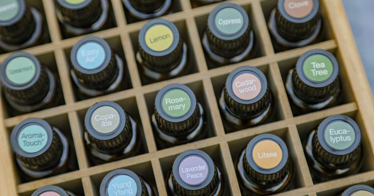 A top-down view of several essential oil bottles stored in a wooden box. Each bottle has a label for a different scent.